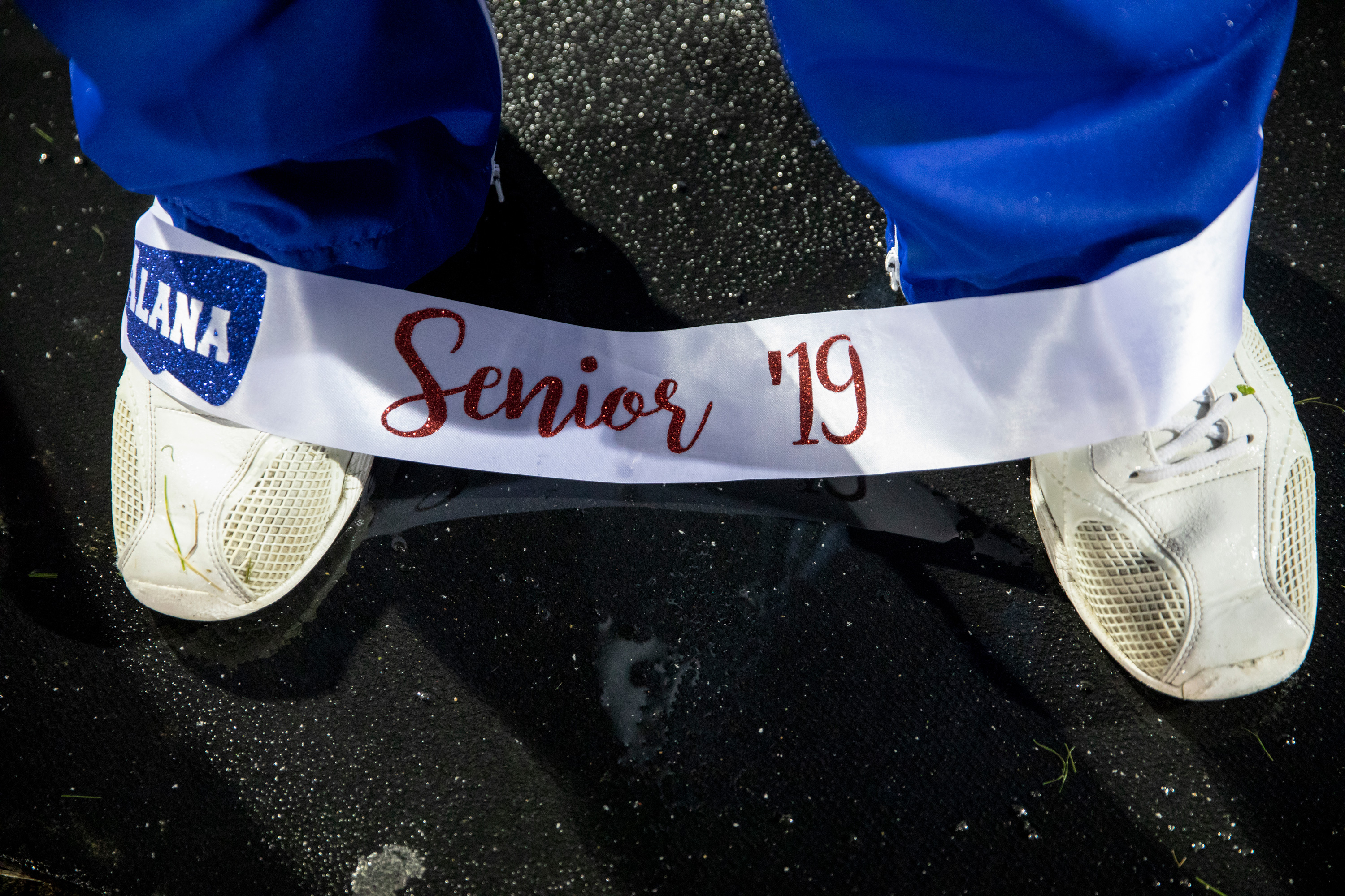 Alana’s senior sash slips from her shoulders as she stands on the sidelines in the drizzling rain ahead of the football game. 